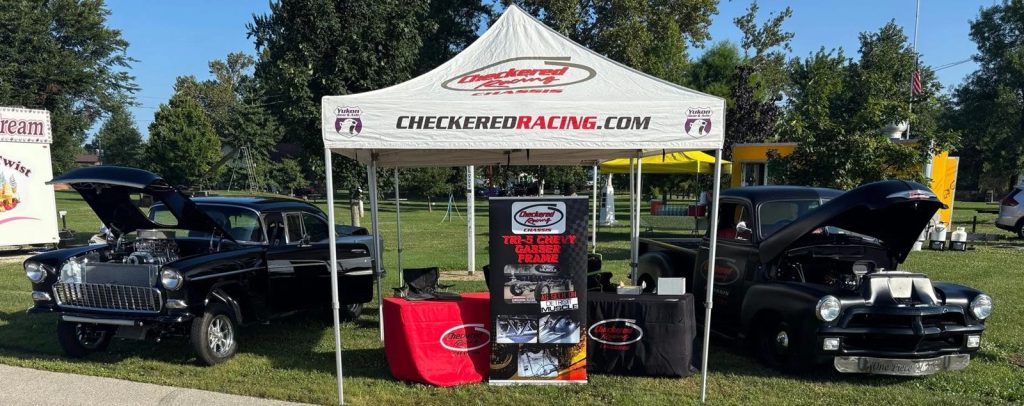 Checkered Racing tent with two black classic Chevrolets at a car show